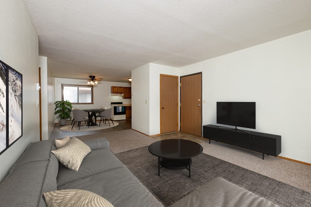 Fargo, ND Gemstone Apartments. A living room with a gray couch and a black coffee table. The dining room is in the background with a 4 chair table.