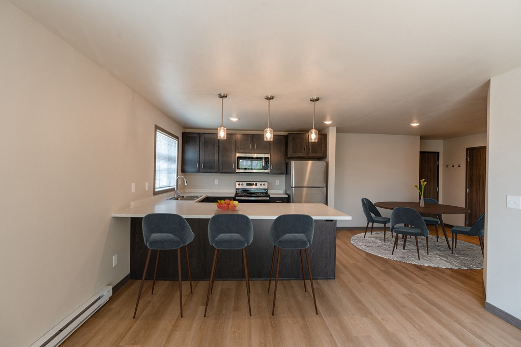 a kitchen with an island with four chairs and a dining room with a table. Fargo, ND Granger Court Apartments