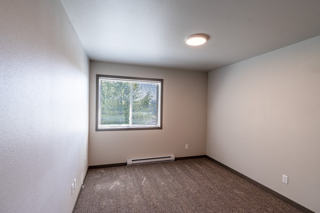 A bedroom with a window and baseboard heater. Fargo, ND Granger Court Apartments.