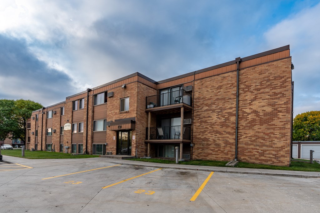 a brick apartment building with a parking lot and a cloudy sky. Fargo, ND Hartford Apartments