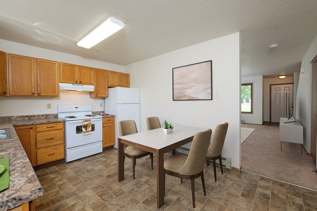 a kitchen with white appliances and a dining table with chairs. Fargo, ND Hazelwood Townhomes