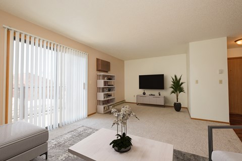 Fargo, ND Hunters Run Apartments. A living room with a tv, coffee table, and bookshelf with a large sliding glass door that brightens up the room with natural light.