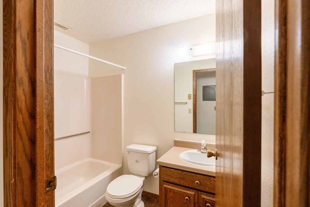 A bathroom with a toilet sink and tub and a mirror. Fargo, ND Huntington Apartments.