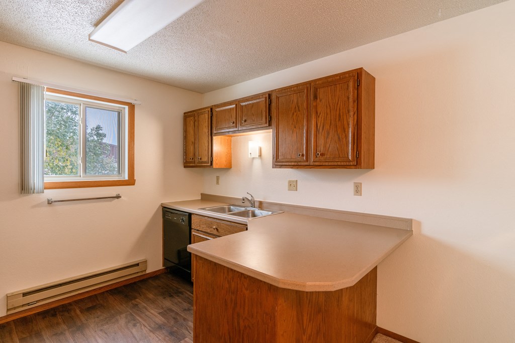 A kitchen with a sink and dishwasher with a window. Fargo, ND Huntington Apartments.