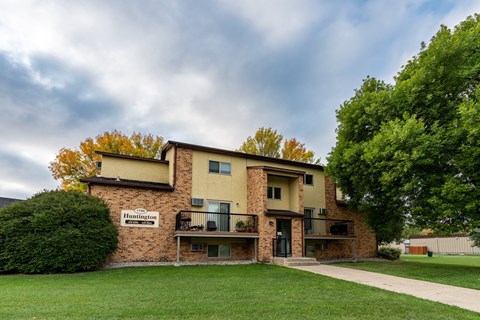 An apartment building with a green yard and a cloudy sky.Fargo, ND Huntington Apartments.