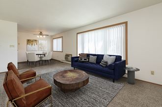 Fargo, ND Islander Apartments. A living room with a blue couch and leather chairs. A large window brightens the room with natural light.