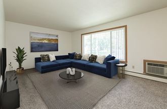 Fargo, ND Islander Apartments. A living room with a large blue couch and a coffee table.  A large window brightens the room with natural light