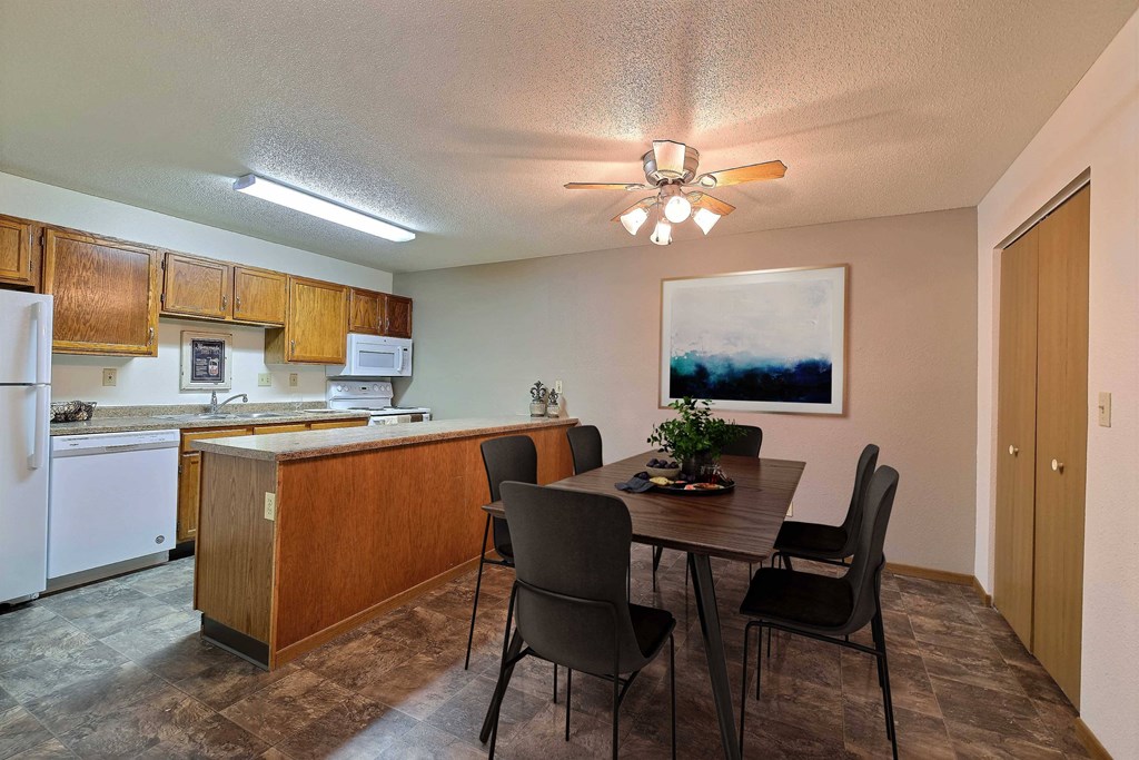 a dining area with a table and chairs and a kitchen in the background. Fargo, ND Kennedy Apartments