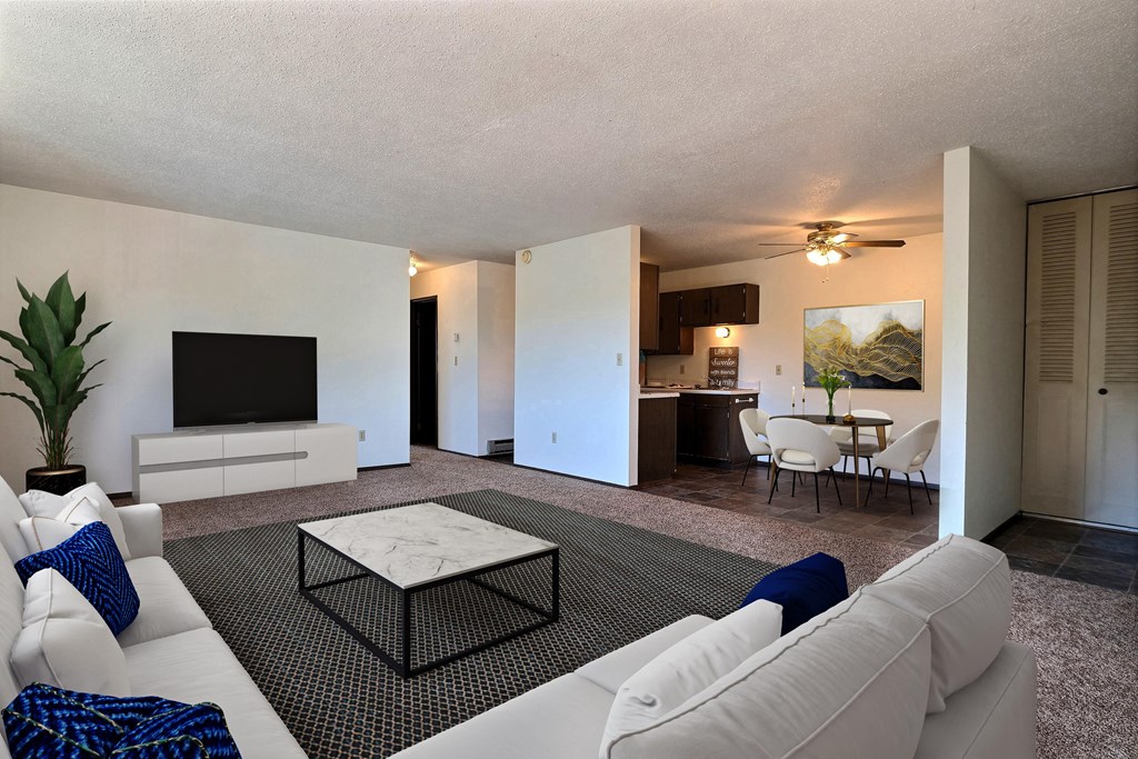 Fargo, ND Kingswood Apartments. A living room with a large white couch, a coffee table, and a tv. The dining room is in the background with a 4 chair table