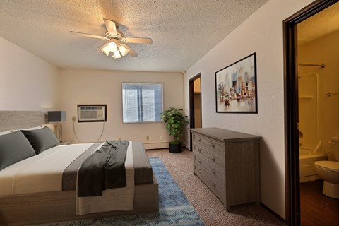 Fargo, ND Kingswood Apartments.  A bedroom with a bed and a dresser a large walk in closet is in the back corner of the room along with a window to brighten the room with natural light