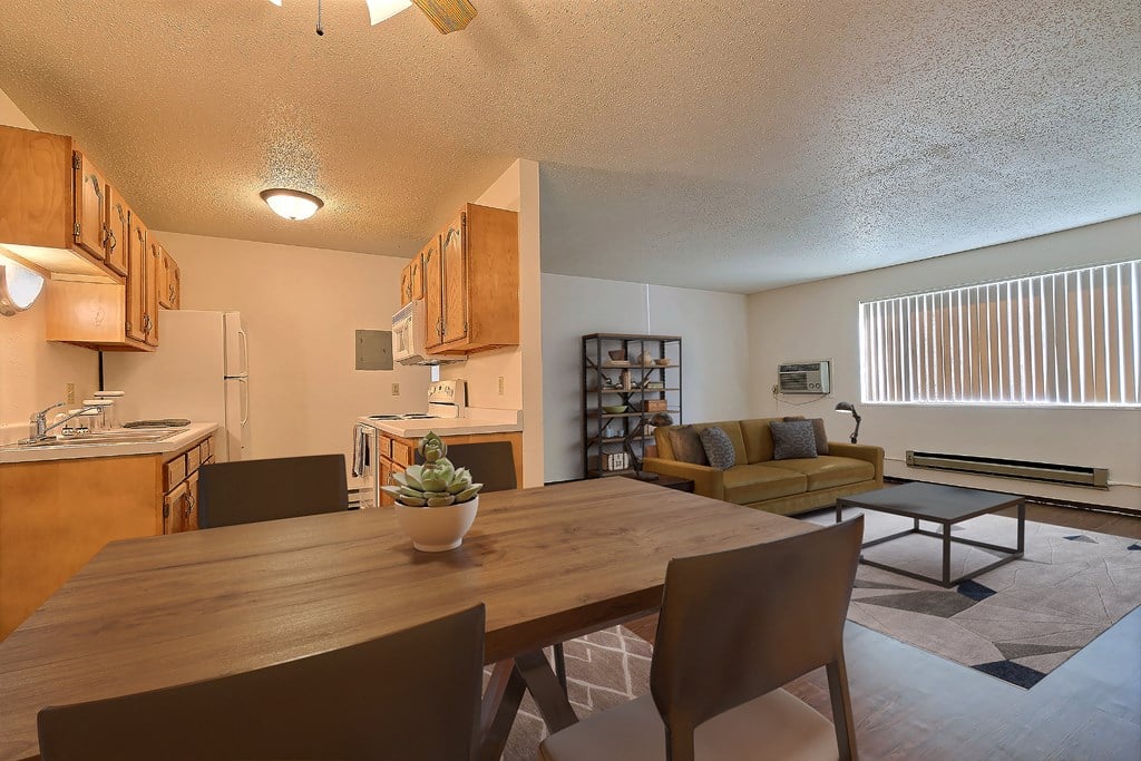 Fargo, ND Kingswood Apartments. A kitchen and living room with a wooden table and four chairs. The kitchen is in the background.