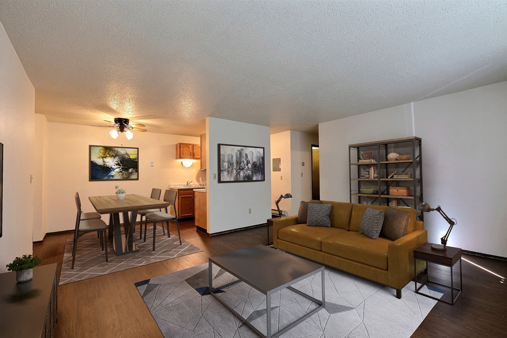 Fargo, ND Kingswood Apartments.  A living room with a dining room and kitchen in the background. The living room has a couch, coffee table, and a large bookshelf behind the couch
