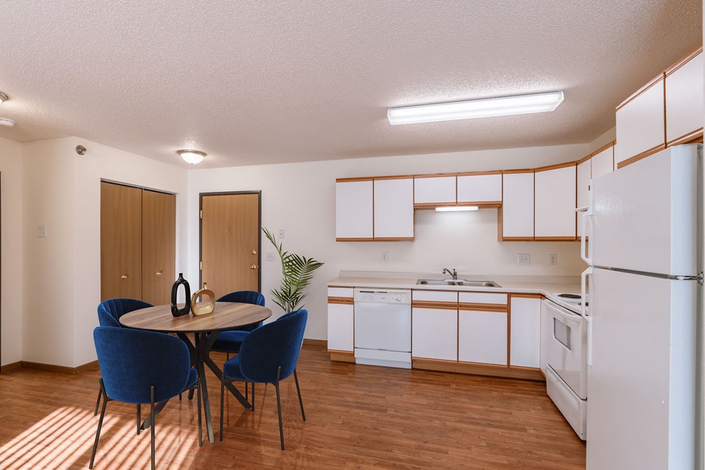 Fargo, ND Lake Crest Apartments | Dining a kitchen with white appliances and a table with chairs. Fargo, ND Lake Crest Apartments