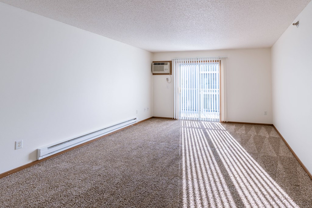 a spacious living room with carpet and a door to a balcony. Fargo, ND Lake Crest Apartments