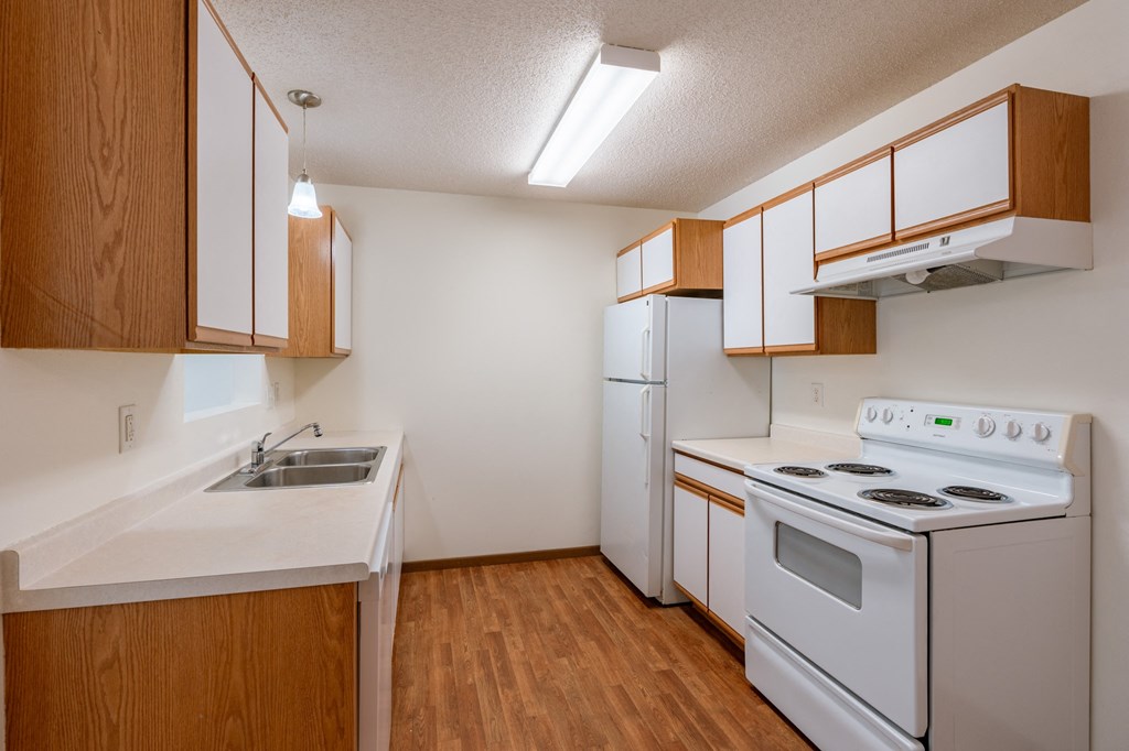 a kitchen with white appliances and wooden cabinets and a white stove. Fargo, ND Lake Crest Apartments