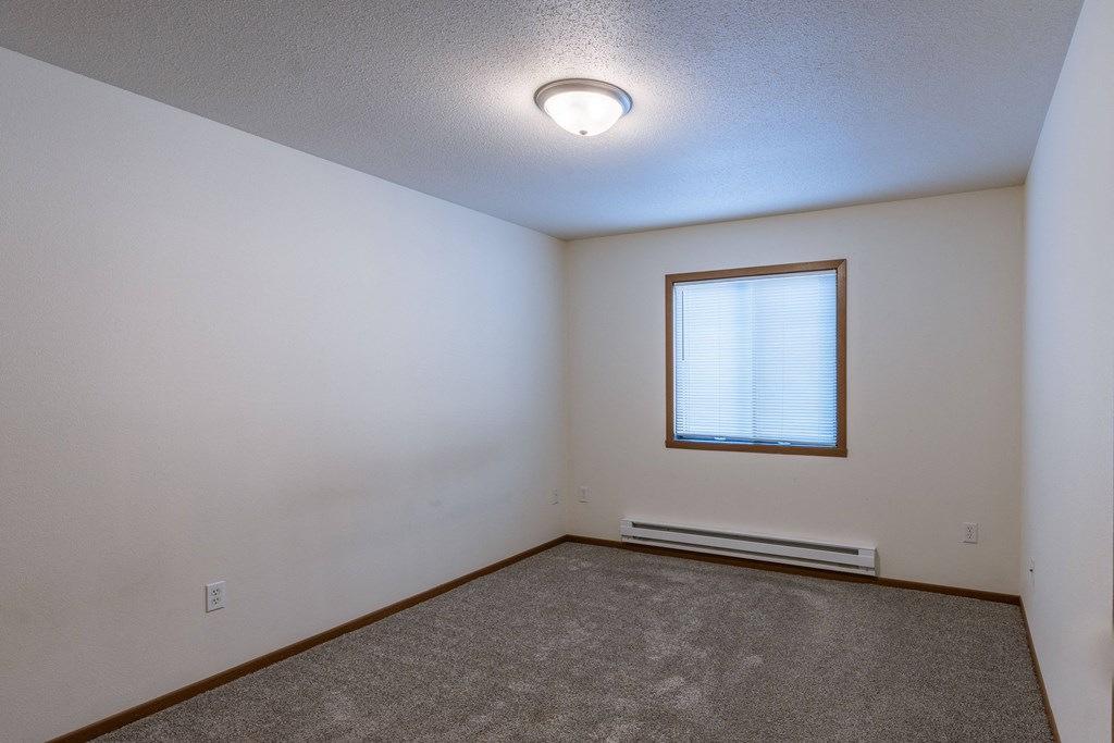 the bedroom of an empty house with carpet and a window. Fargo, ND Lake Crest Apartments