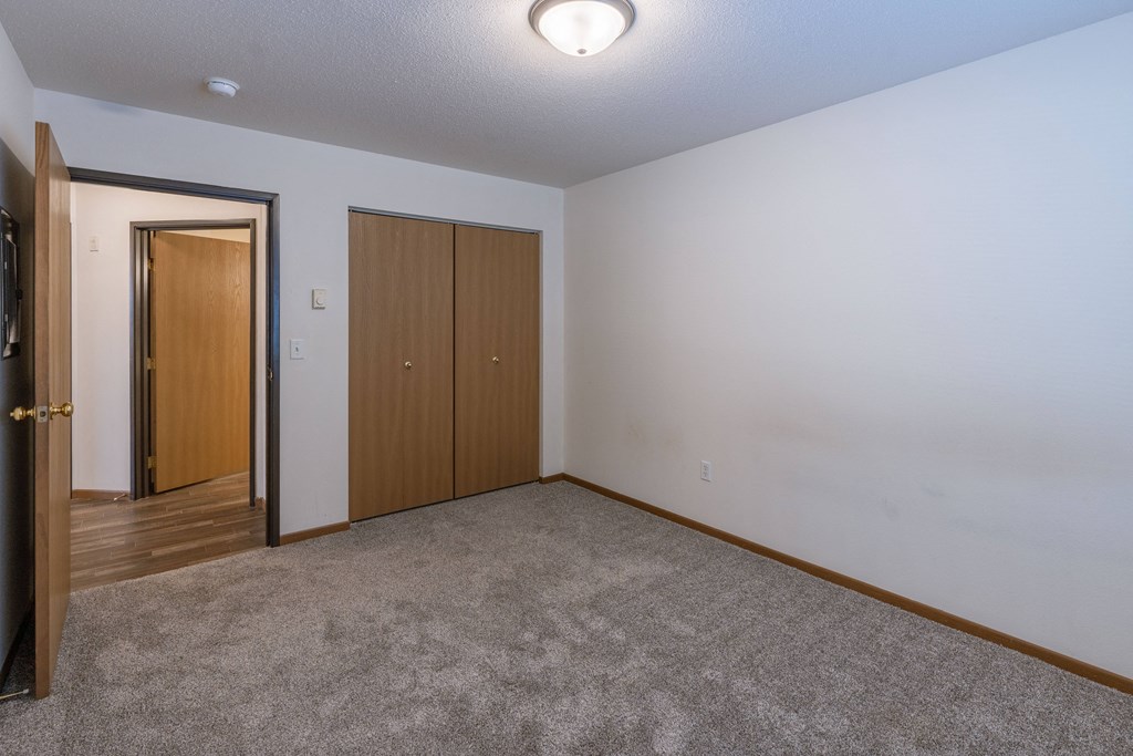 a bedroom with carpet and a door to a closet. Fargo, ND Lake Crest Apartments