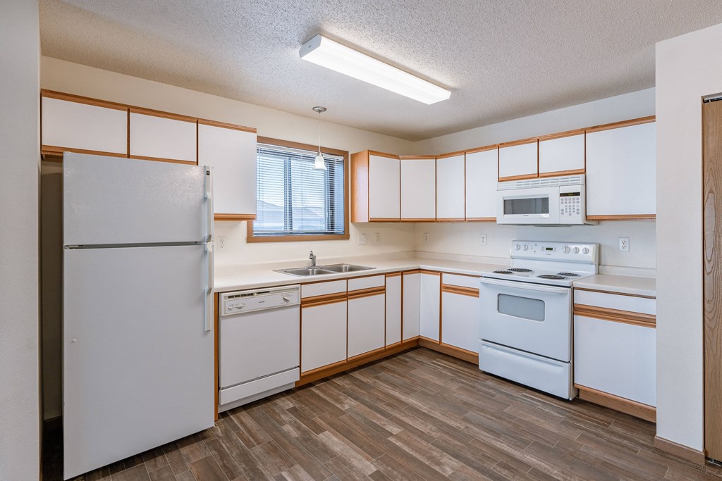 an empty kitchen with white appliances and white cabinets. Fargo, ND Lake Crest Apartments