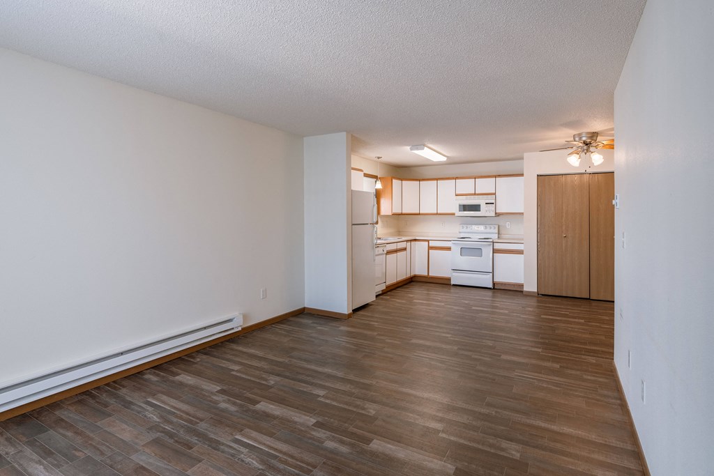 an empty living room and kitchen with wood flooring and white cabinets. Fargo, ND Lake Crest Apartments