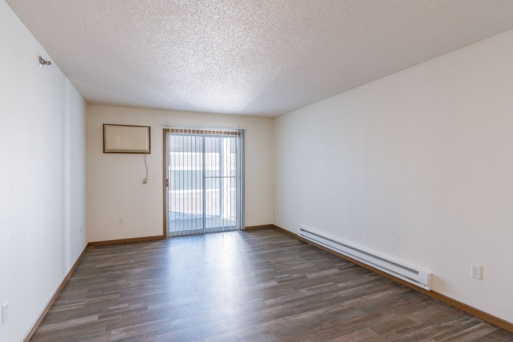 an empty living room with wood flooring and a sliding glass door. Fargo, ND Lake Crest Apartments
