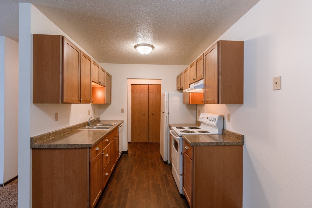 A kitchen with wooden cabinets and a white stove and refrigerator. Fargo, ND Long Island Apartments.