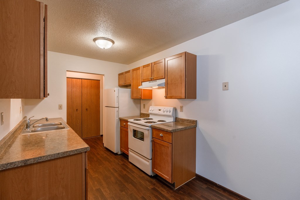 A kitchen with wooden cabinets and white appliances and a sink. Fargo, ND Long Island Apartments.