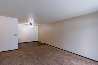 An empty living room with carpet and white walls with a dining room in the background. Fargo, ND Long Island Apartments.