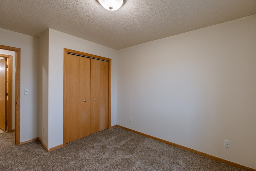 a bedroom with a closet and a door to a hallway. Moorhead, MN Mallard Creek Apartments