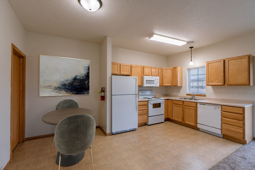 a kitchen with white appliances and wooden cabinets and a table. Moorhead, MN Townhomes at Mallard Creek