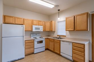a kitchen with white appliances and wooden cabinets and a window above the sink. Moorhead, MN Mallard Creek Apartments