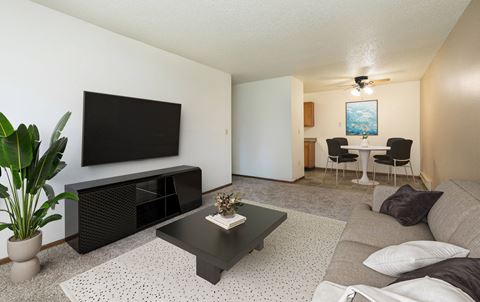 a living room with a coffee table and tv with a dining room in the background. Fargo, ND Maplewood Bend Apartments