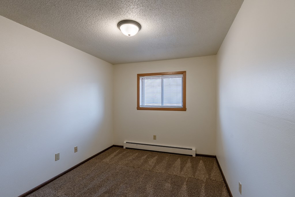 a bedroom of an empty house with a window and white walls. Fargo, ND Martha Alice Apartments