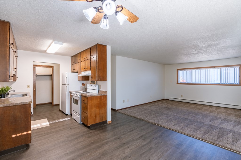 an empty living room with a kitchen and a ceiling fan. Fargo, ND Martha Alice Apartments