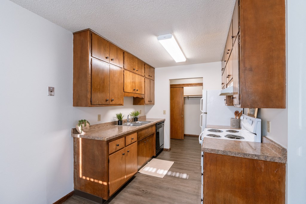 a kitchen with wooden cabinets and a white stove and refrigerator. Fargo, ND Martha Alice Apartments