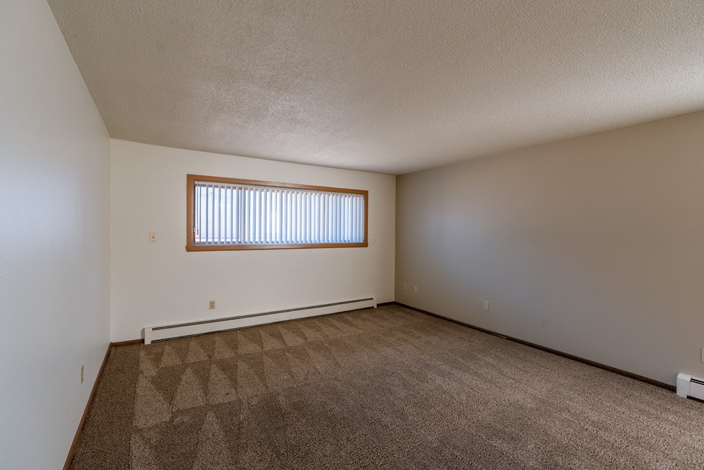 an empty living room with carpet and a window. Fargo, ND Martha Alice Apartments