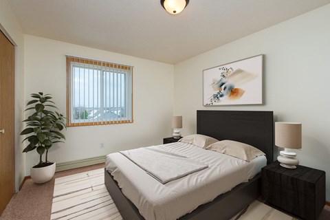 a bedroom with a bed and a potted plant and a window. Fargo, ND Maybrook Apartments