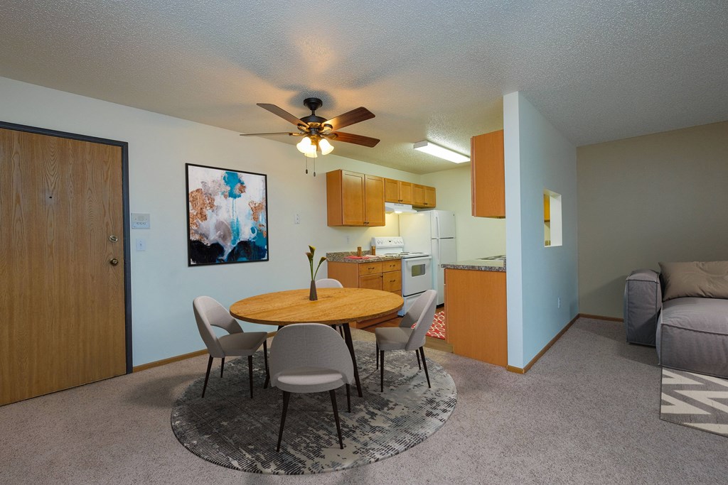 a living room with a dining room table and a kitchen. Fargo, ND Maybrook Apartments