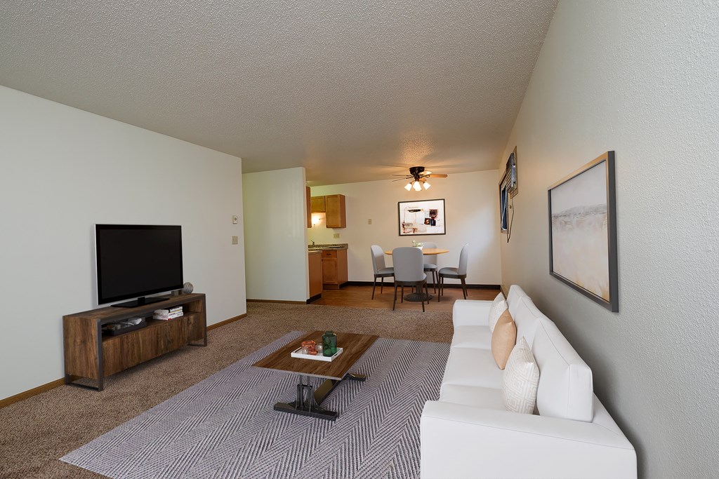 Fargo, ND Monticello. A living room with a couch a coffee table and a tv. The dining room in the background with a four chair table and a fan above it.