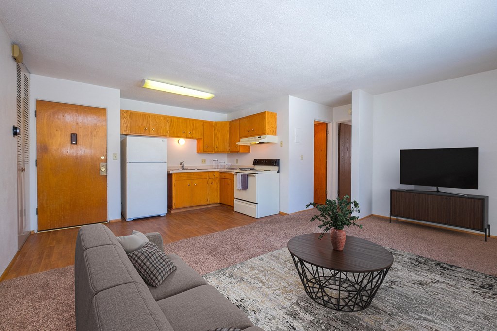 Fargo, ND Morningside Apartments. A living room with a couch and a coffee table. Theres a small kitchen in the background with white appliances.