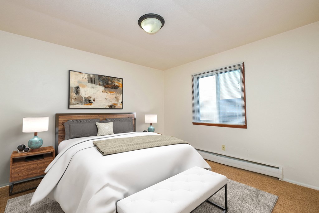 a bedroom with a white bed and a white couch. Fargo, ND North Manor Apartments