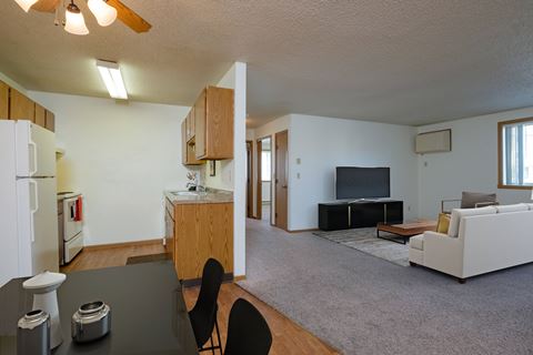 a view of a living room and a kitchen with a couch and a tv. Fargo, ND Oak Court Apartments