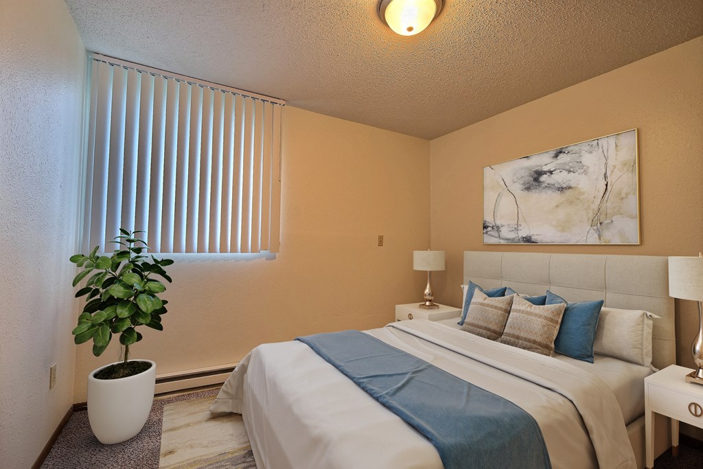 a bedroom with a large bed and a potted plant. Fargo, ND Pacific Park 2 Apartments.