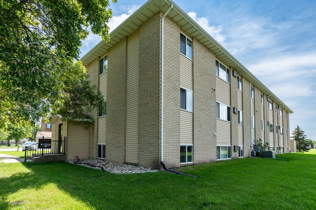 a brick building with green grass and a tree. Fargo, ND Park Circle Apartments.