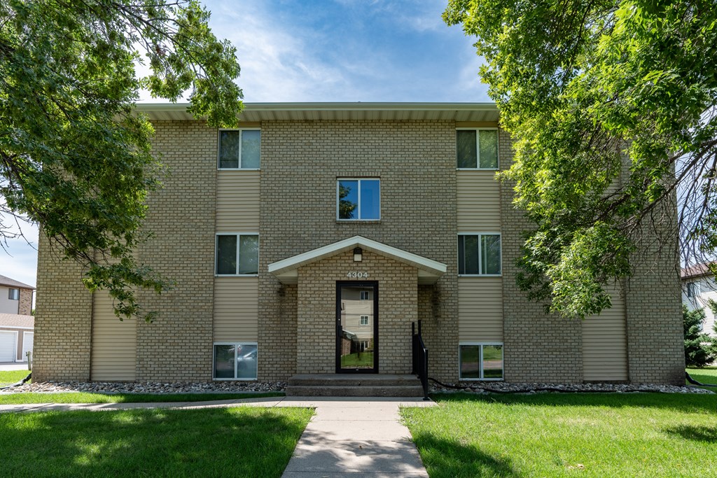 a brick building with a sidewalk in front of it and trees. Fargo, ND Park Circle Apartments.