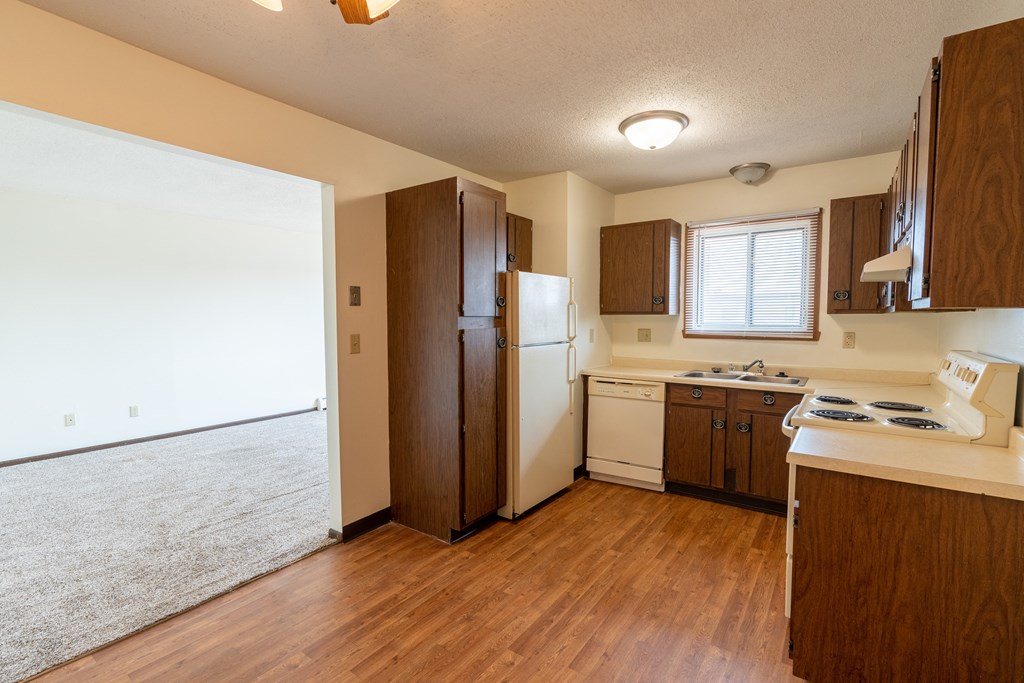 Kitchen with white appliances and brown cabinets a small window above the sink brightens the room with natural light at Parkwest Gardens West Fargo, ND