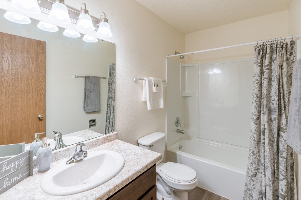 Fargo, ND Patricia Ann Apartments. A bathroom with a white bathtub and a white toilet next to a sink with a mirror