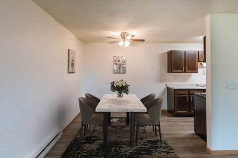 a dining room with a table and chairs and a kitchen with a ceiling fan. Fargo, ND Patricia Ann Apartments