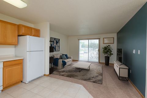 A kitchen and living room with a refrigerator and a sliding glass door. Fargo, ND Pinehurst Apartments.