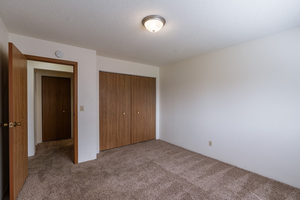 an empty living room with carpet and a door to a closet. Fargo, ND Place One Apartments
