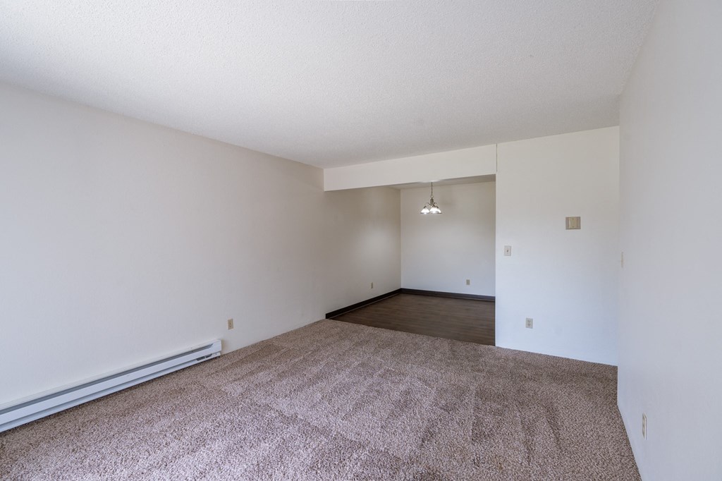 the living room and dining room of an apartment with carpet and white walls. Fargo, ND Place One Apartments